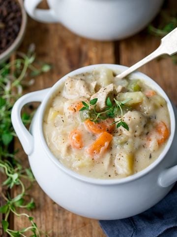 Chicken pot pie soup in a white bowl with fresh thyme on top.
