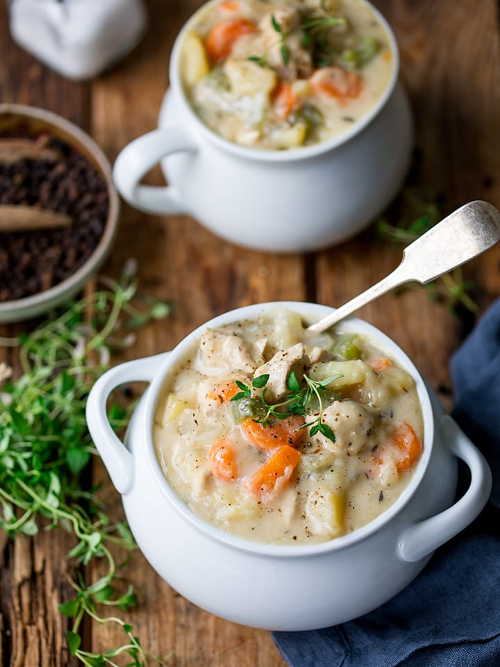 Chicken pot pie soup in a white bowl with thyme on top. 