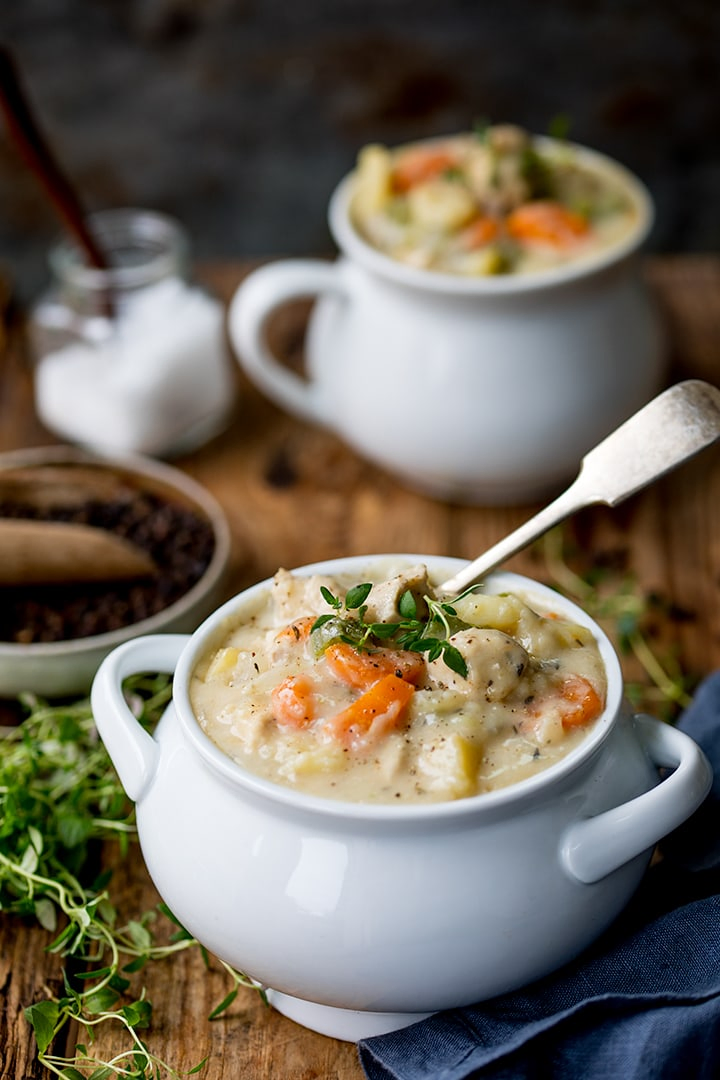 Chicken pot pie soup in a white bowl on a wooden board.