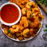 Plate of coconut shrimp with a bowl of sweet and sour sauce nestled in. Plate is on a grey background.