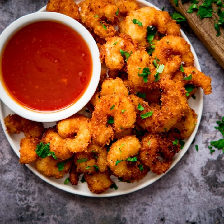 Plate of coconut shrimp with a bowl of sweet and sour sauce nestled in. Plate is on a grey background.