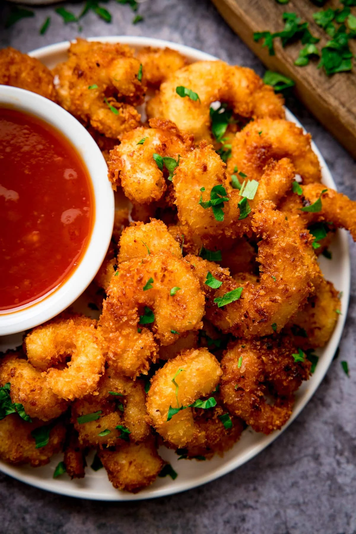 Coconut prawns on a plate on a grey background. Dish of sweet and sour sauce is next to the prawns.