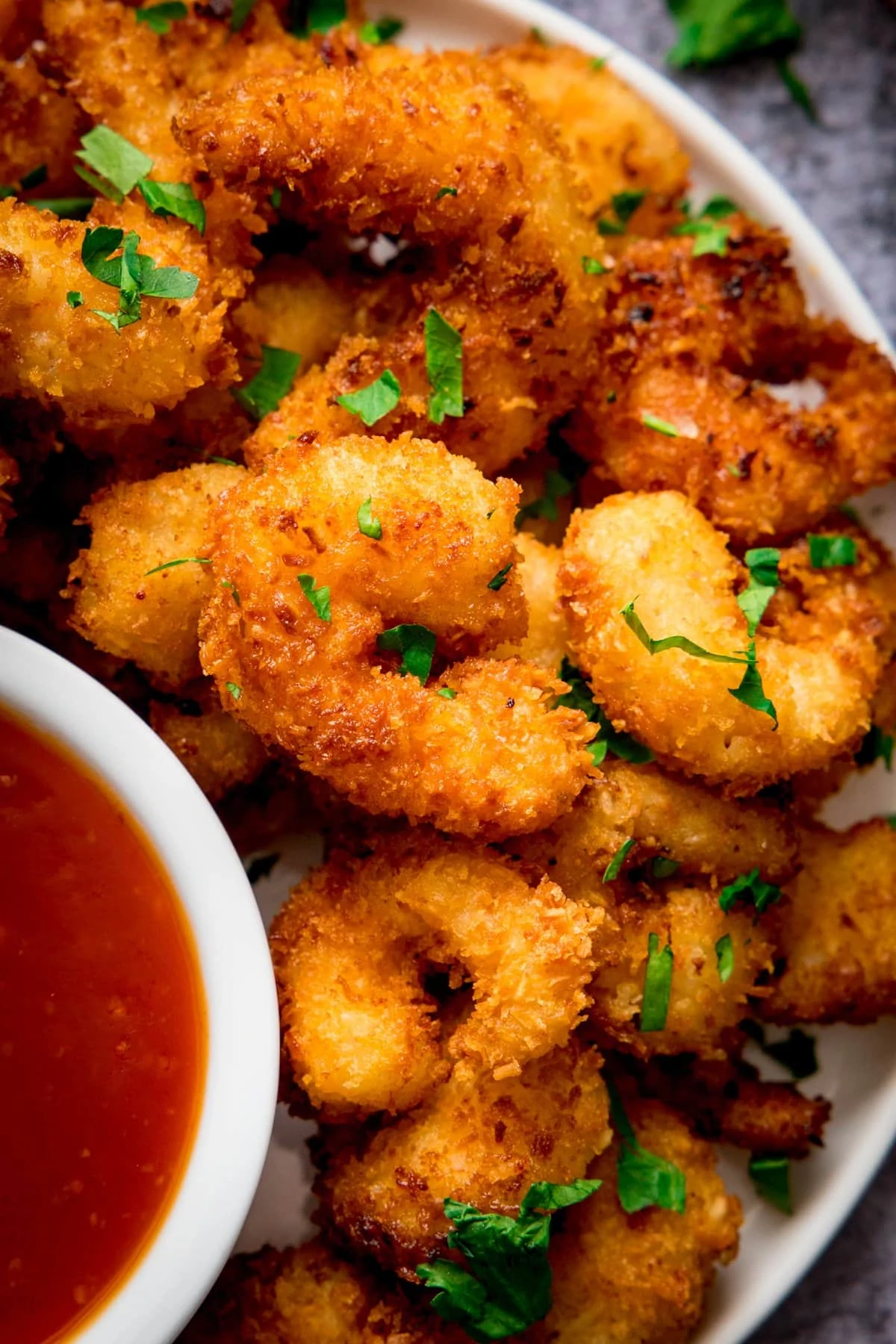 Close up of coconut shrimp on a plate next to a dish of sweet and sour sauce.