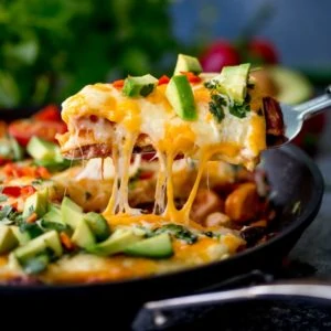 Slice of chicken enchilada skillet lasagna being lifted from the pan. Cheese is stretching.