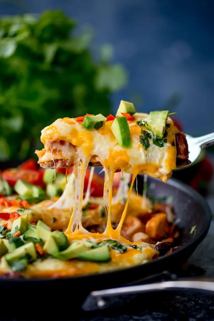 Slice of chicken enchilada skillet lasagna being lifted from the pan. Cheese is stretching.