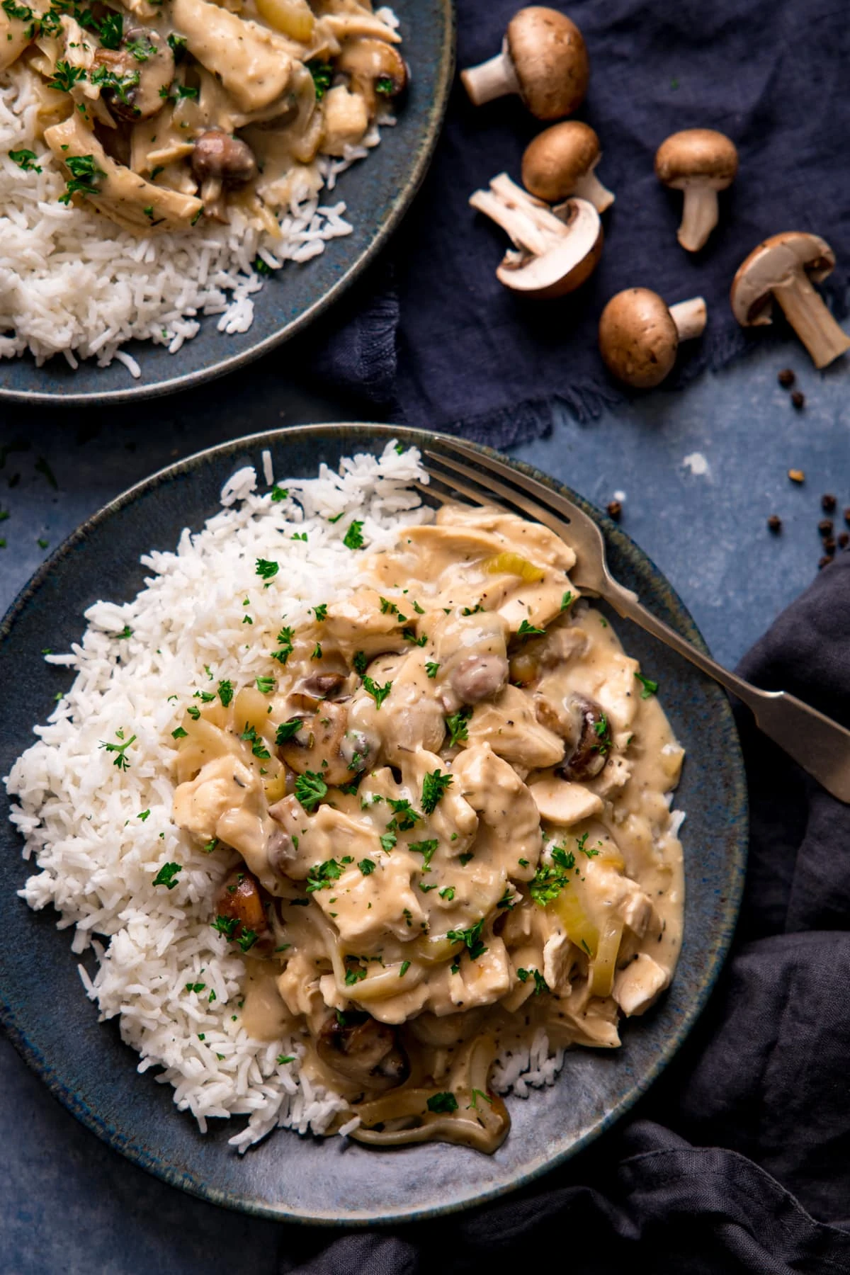 Chicken ala king with rice on a dark blue plate. Further plate in the background.