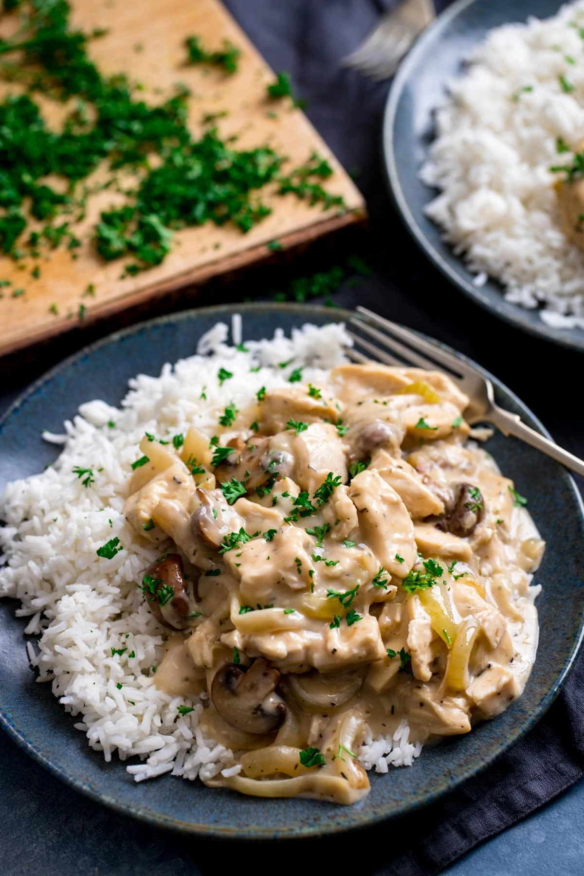 Chicken ala king on a plate with rice. Chopped parsley on a board in the background and on the dish too.