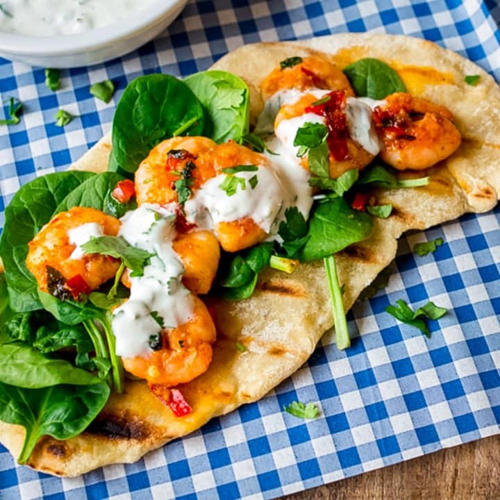Garlic chilli prawns with spinach and yogurt dip on homemade flatbread on a piece of blue chequered paper
