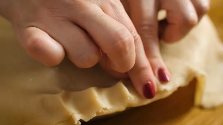Fingers pinching the pastry edge to make a decorative crusty