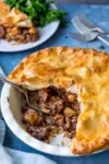 Large steak and potato pie with slice taken out.