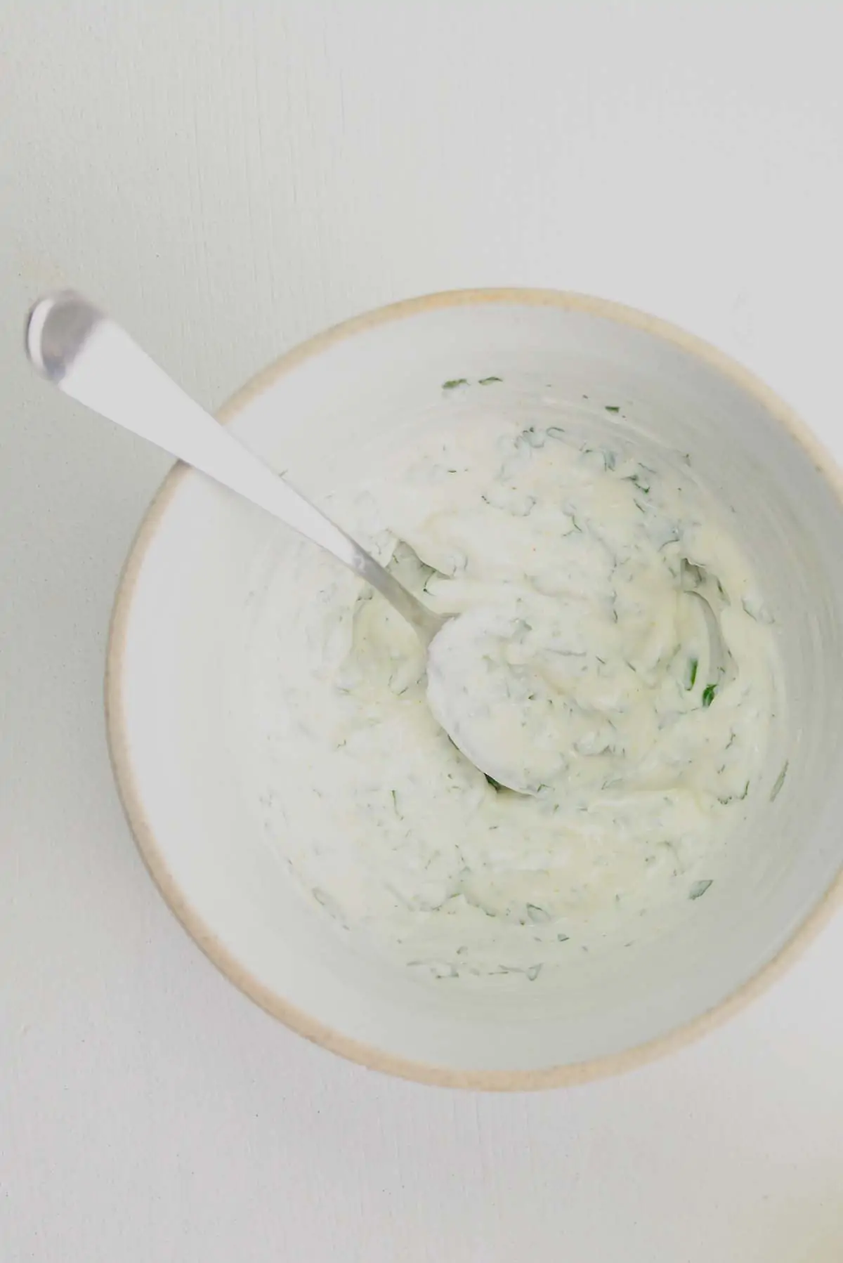 Overhead image of yogurt dip in a white bowl on a white surface