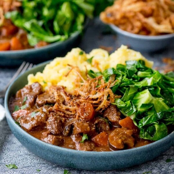 Square image of a bowl of beef and Guinness Stew with mashed potatoes and green cabbage