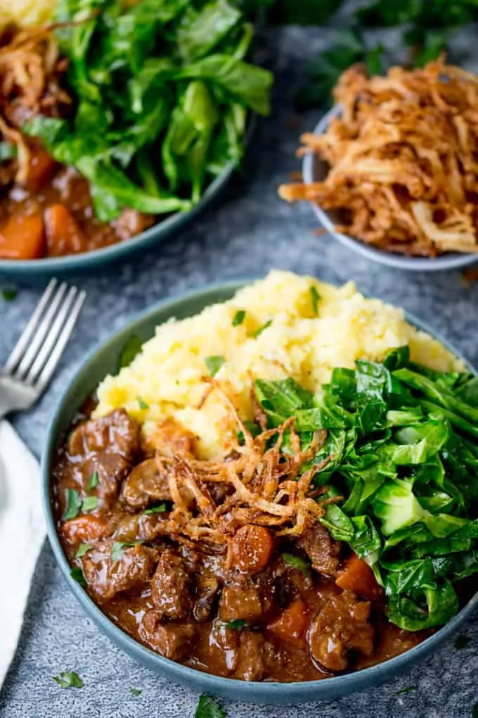 Bowl of beef and Guinness stew with mashed potato, greens and crispy onions.
