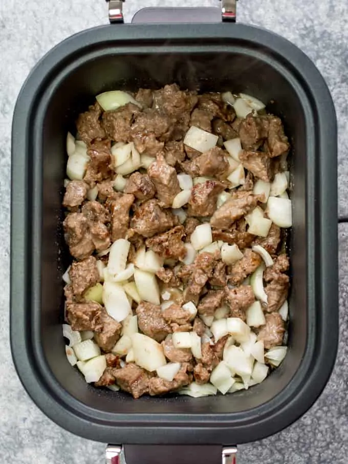 Crockpot filled with seared beef and onions