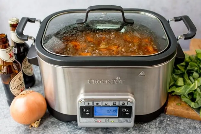 Crockpot with beef stew. Onions, Guinness and cabbage on the table.