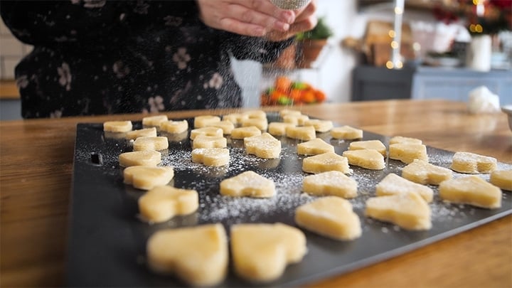 uncooked shortbread hearts on a tray with icing sugar being sprinkled on