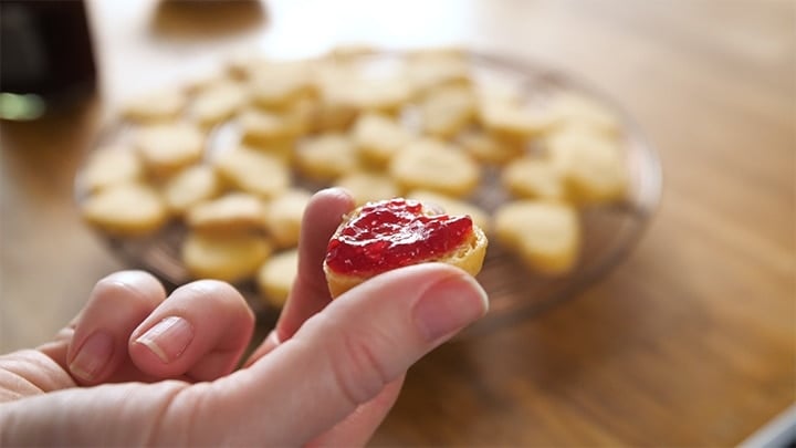 Hand holding mini shortbread heart with jam spread on
