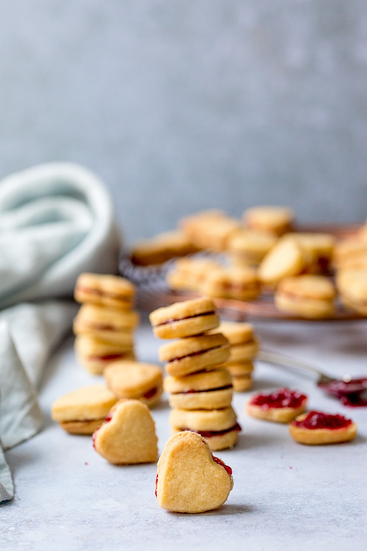 Stack of heart shaped valentine shortbread cookies with jam in the middle, plus extra cookies scattered around
