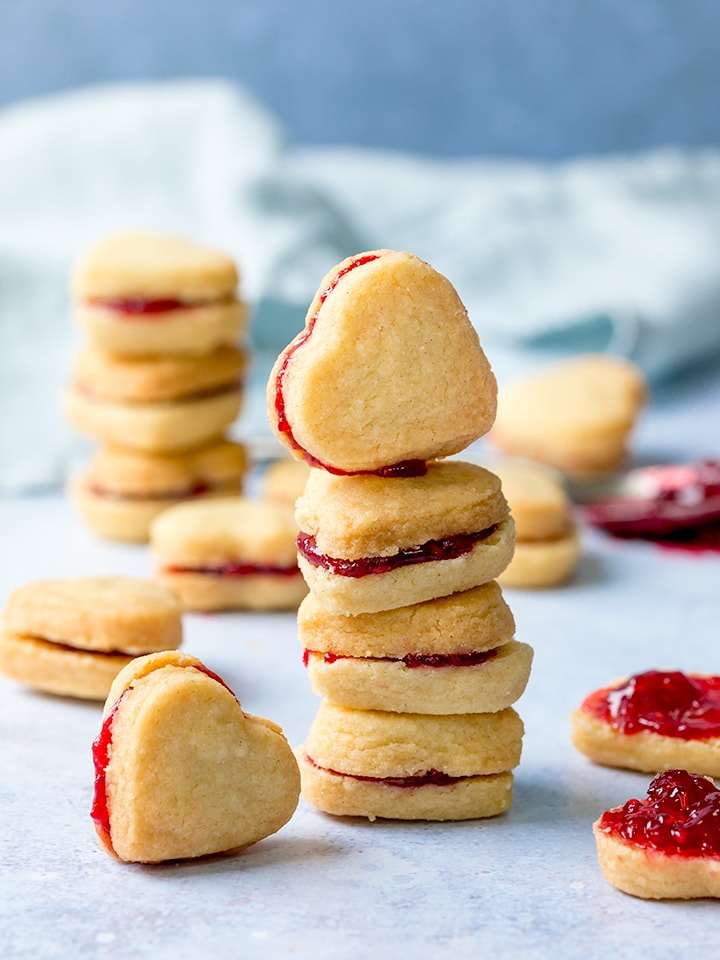Stack of jam-filled, heart-shaped valentine shortbread cookies on a light blue background