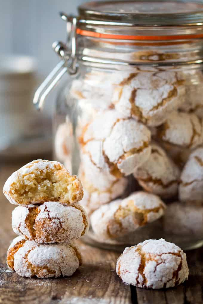 Italian Amaretti cookies on a wooden board against a dark background. Coffee being poured in background.