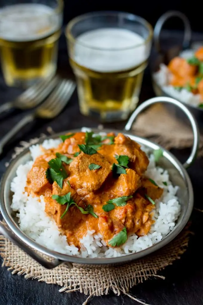 A metal bowl with rice and Crock Pot Butter Chicken with 2 beers in the background