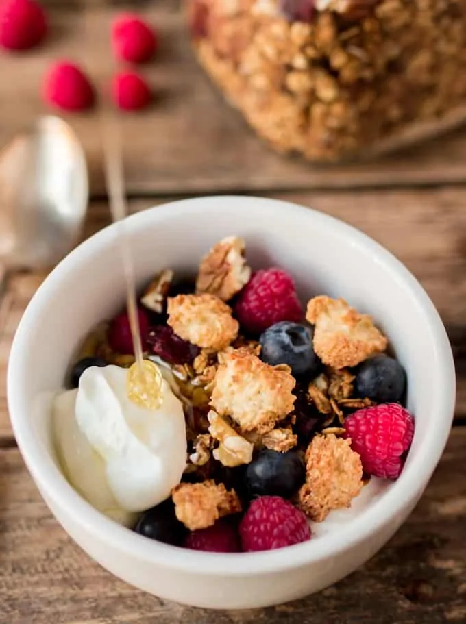 Bowl of Coconut Macaroon Granola with Greek yogurt and honey being poured onto