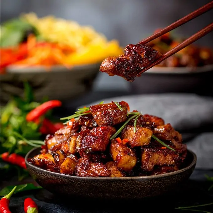 Bowl of chinese sticky pork belly with bowl of stir fried vegetables in the background.