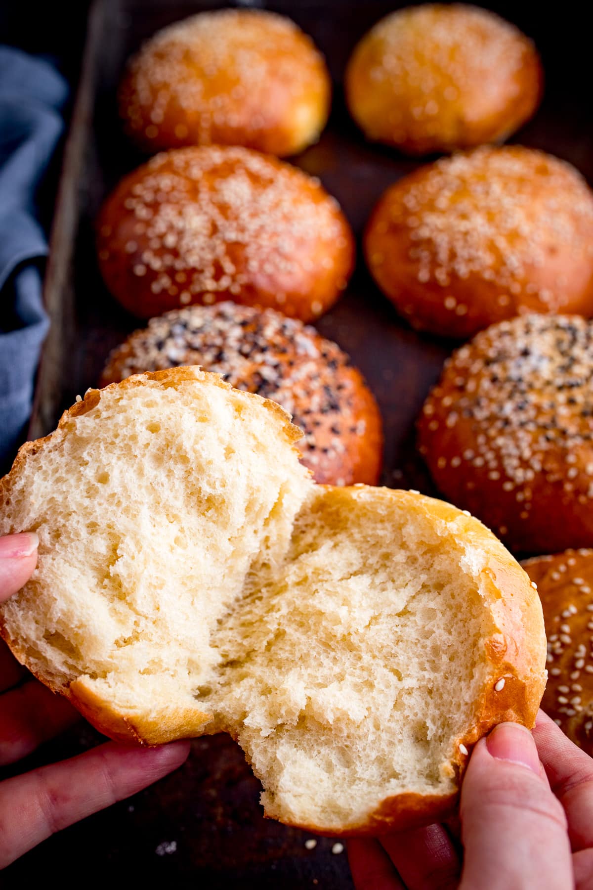 seeded brioche buns on a tray with one bun being opened by two hands