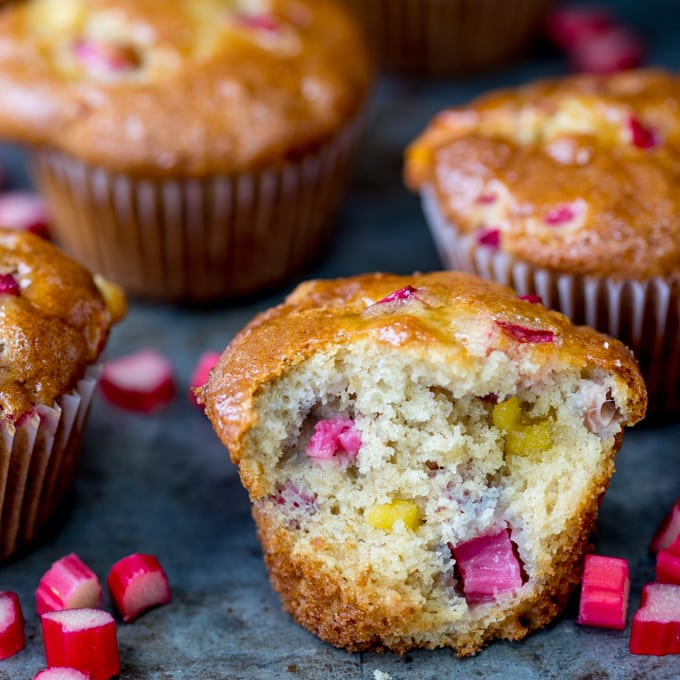 Glazed muffin with rhubarb and marzipan chunks. Bite taken out of muffin. Further whole muffins in the background.