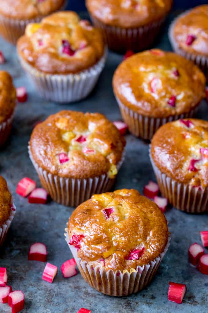 Worn steel background with rhubarb and marzipan muffins. Pieces of chopped rhubarb scattered around muffins.