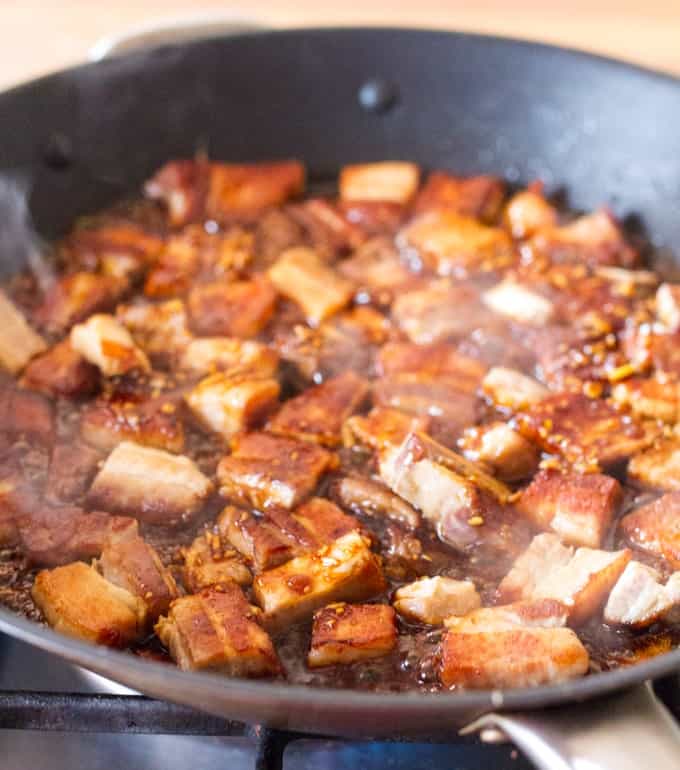 Chunks of pork belly frying in a pan with a chinese sticky glaze