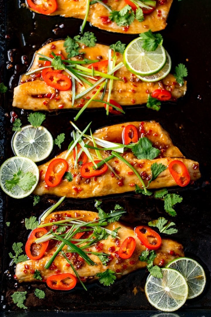 Sticky Asian-style baked seabass fillets on a tray with chillies, spring onion and lime