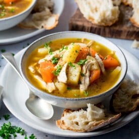 chicken and vegetable soup in a light bowl with bread and spoon on the side