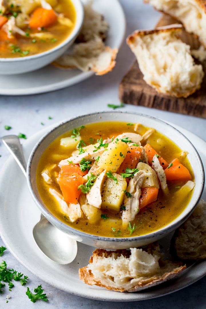 Bowl of chicken and vegetable soup with bread on the side