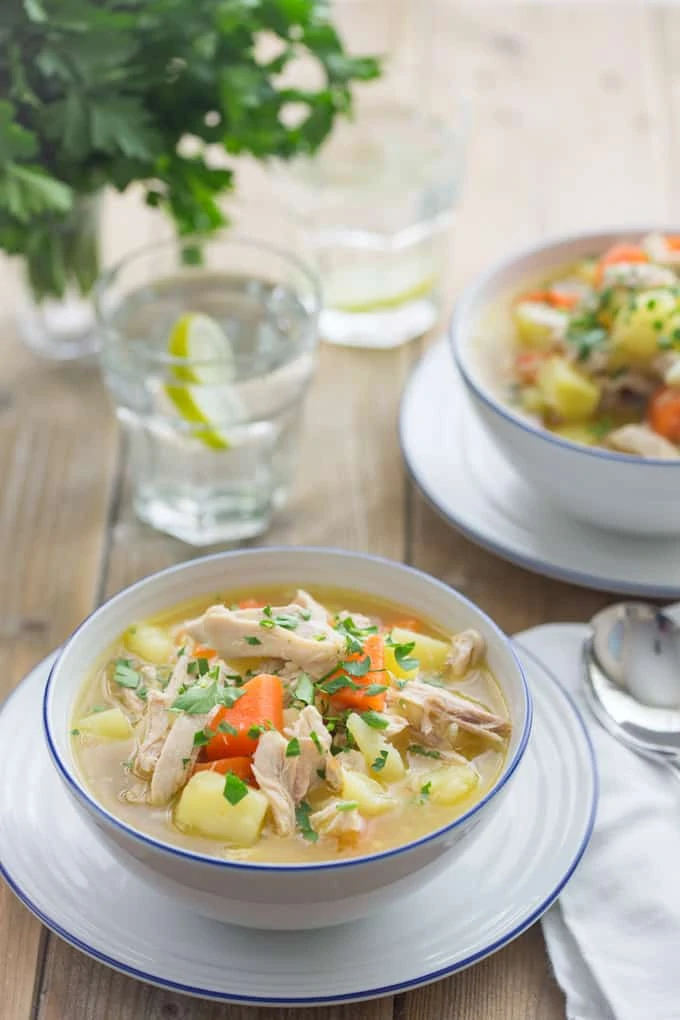 Bowl of chicken and vegetable soup with bread on the side