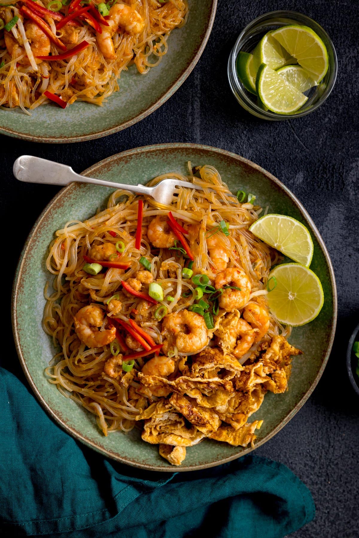 Mee Siam fried noodles on a green plate on a dark background. Further plate just in shot at the top of the frame.