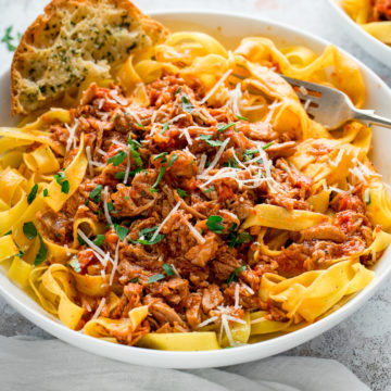 slow cooked pork ragu in a white bowl with pasta and garlic bread