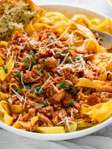 slow cooked pork ragu in a white bowl with pasta and garlic bread