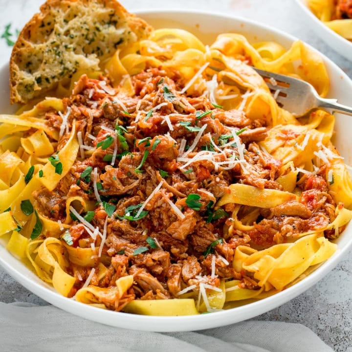 slow cooked pork ragu in a white bowl with pasta and garlic bread
