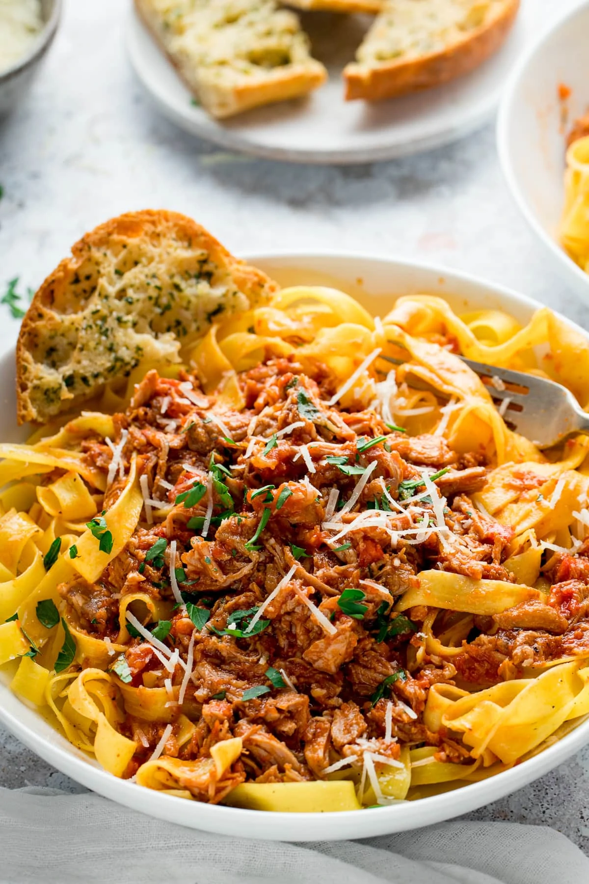 slow cooked pork ragu on top of tagliatelle in a white bowl with garlic bread