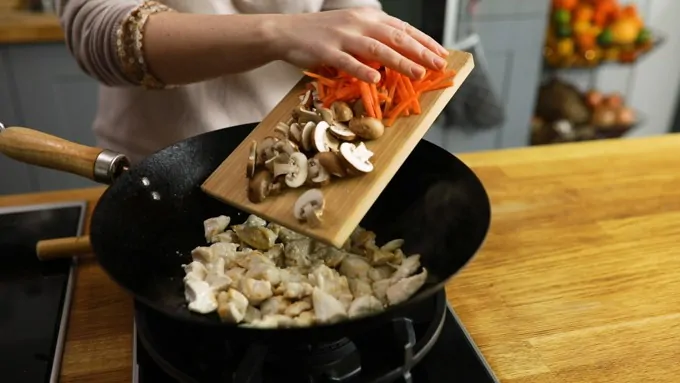 Adding mushrooms and carrot to a wok with Chicken pieces