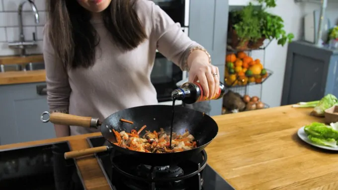 Pouring soy sauce into a wok will Asian chicken and vegetables