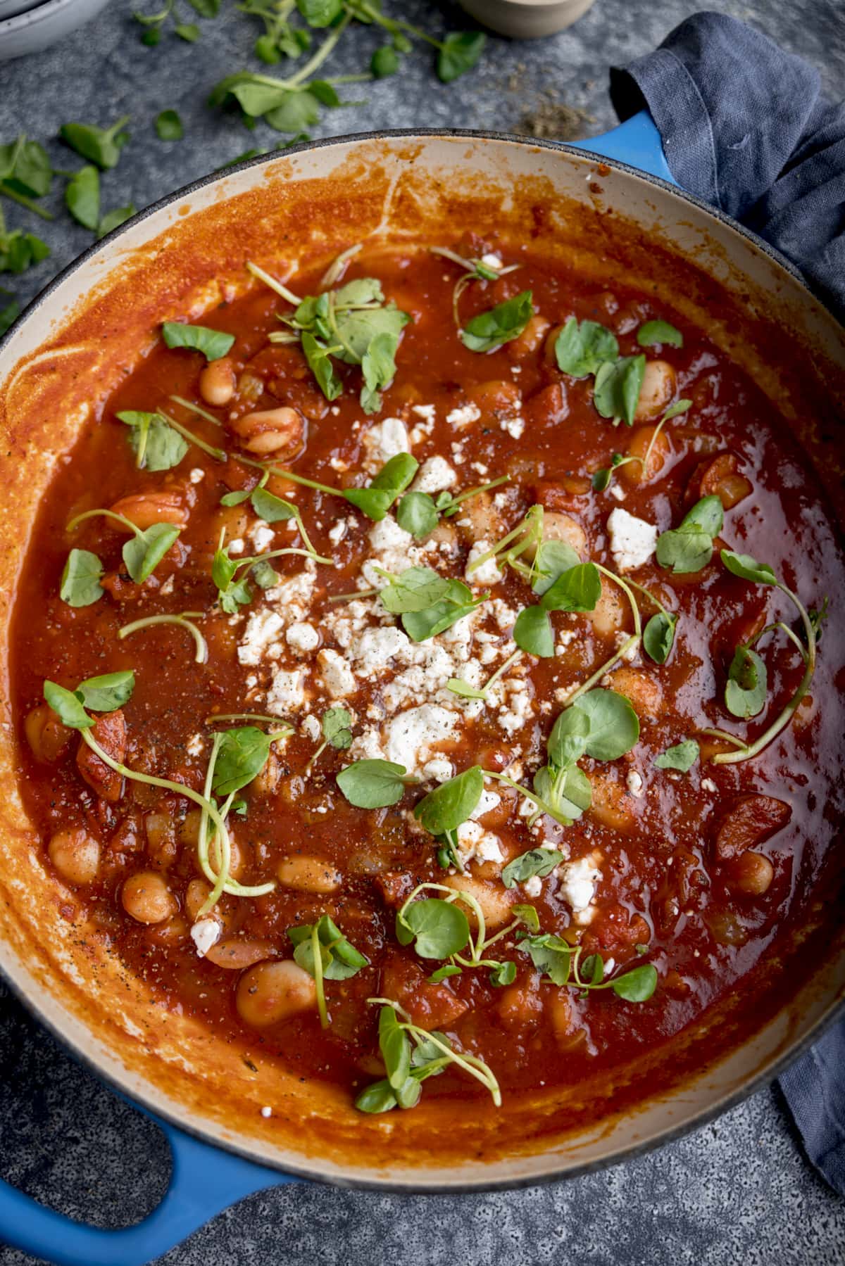 Overhead image of a blue cast iron pan filled with butterbean and chorizo soup. The pan on on a grey background.