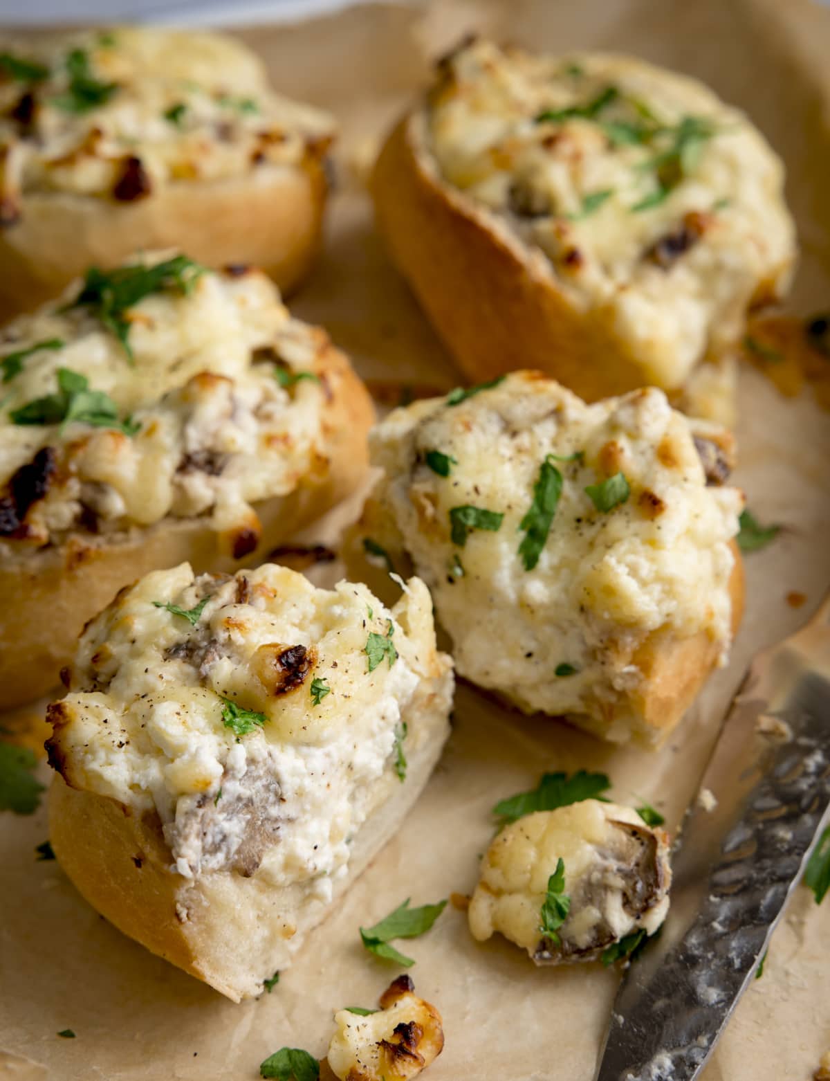 Cheesy Mushroom Stuffed Garlic Breads topped with parsley on a tray. The stuffed bread closest to the front has been sliced in half.