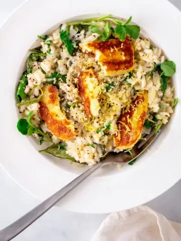 Overhead Picture of lemon risotto topped with fried haloumi slices in a white bowl.