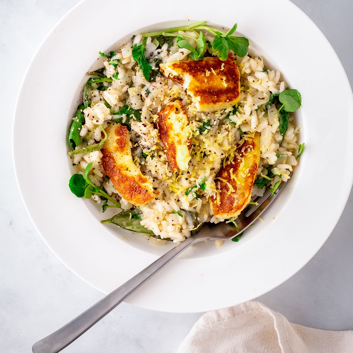 Overhead Picture of lemon risotto topped with fried haloumi slices in a white bowl.