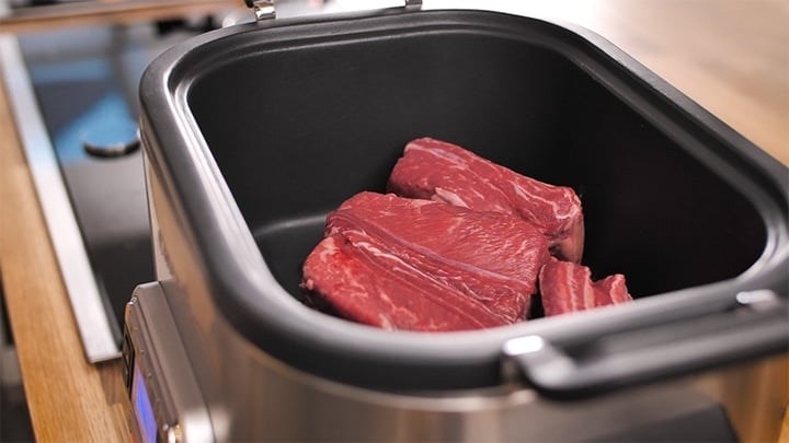 Raw short ribs in a slow cooker being browned