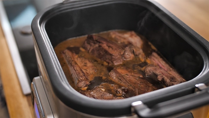 Short ribs simmering in stock and red wine in a slow cooker