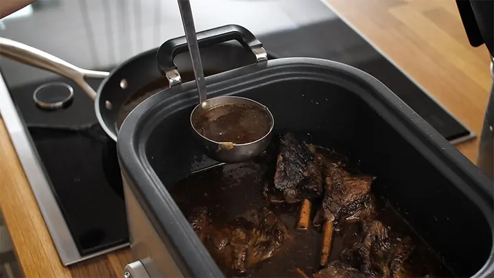 Removing stock using a ladle from a slow cooker with shortribs