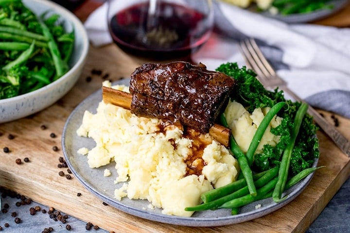 Wide image of slow cooker short ribs served on mashed potatoes